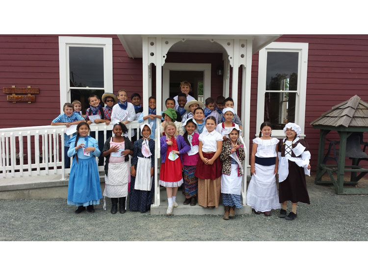 Students in front of one-room schoolhouse with School Marm
